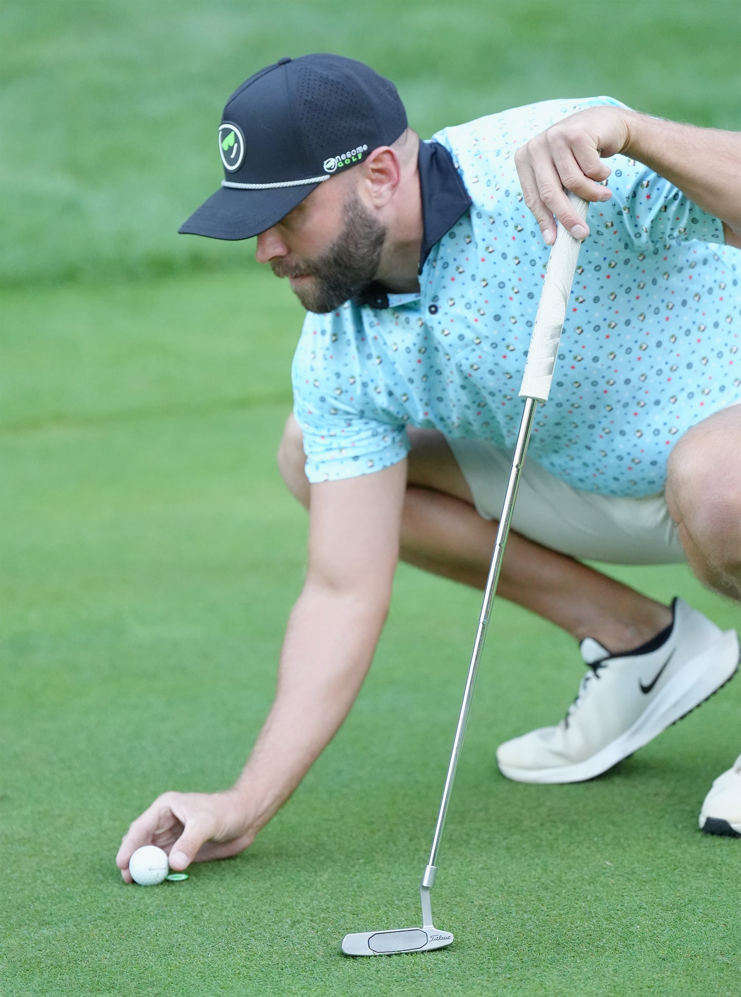 Man wearing black Onesome golf hat placing his golf ball on the green