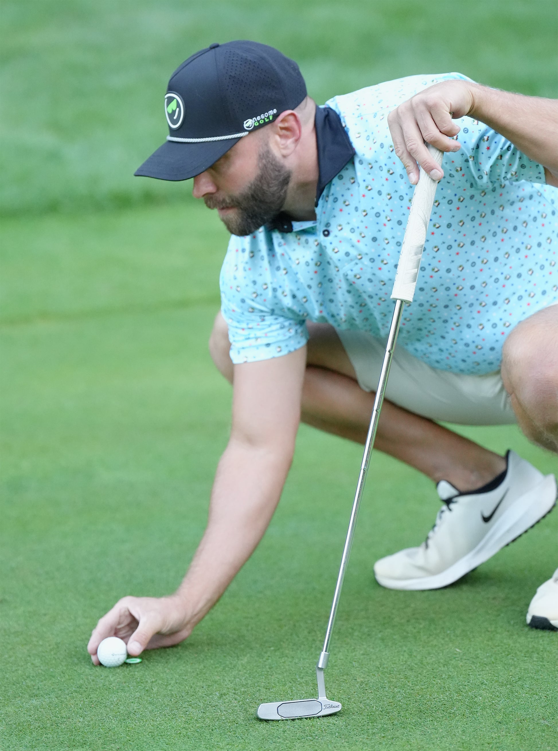 Man wearing black Onesome golf hat placing his golf ball on the green