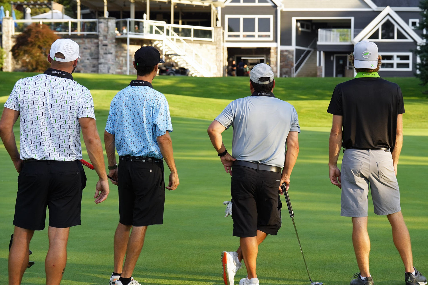 Four men wearing Onesome apparel on a golf course with a clubhouse in the background